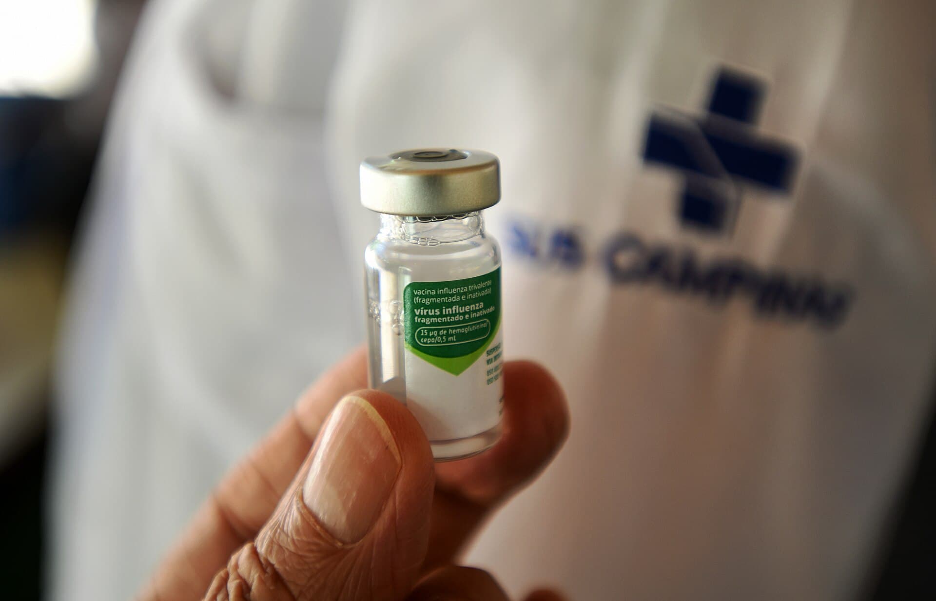 A hand holding a vial of flu vaccine